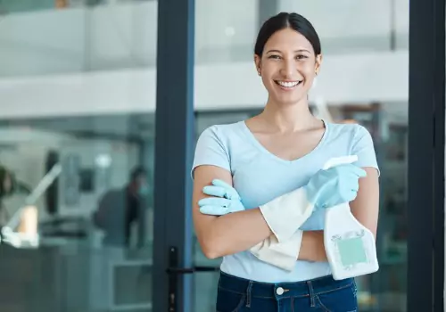 Female smiling outside window and holding cleaning bottle during vacant residential cleaning in Peoria IL.