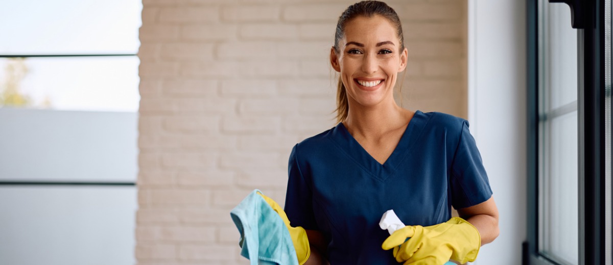 A professional cleaner from Pro Kleen, a commercial cleaning company, smiles while holding a cloth and spray bottle