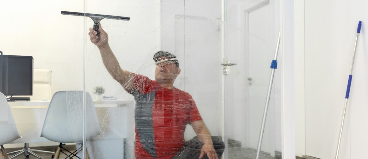 A professional cleaning service worker from Pro Kleen, which offers office & janitorial cleaning services, washes an office glass window