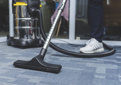 Office Cleaning Services Peoria IL, A man cleans the carpet flooring of an office with an upright vacuum cleaner with an attached upholstery nozzle