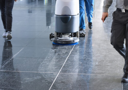 Office Cleaning Services Bloomington IL, A floor cleaning machine in operation on a shiny black tile floor, with people walking nearby