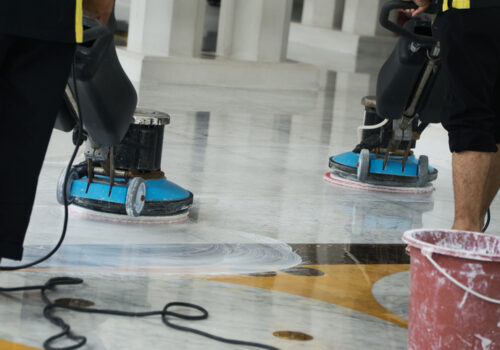 Two workers operate buffing machines to thoroughly clean a polished marble floor, ensuring it maintains its professional and spotless appearance. Equipment and accompanying cleaning supplies are visible, emphasizing a high standard of cleanliness, Janitorial Services Peoria IL