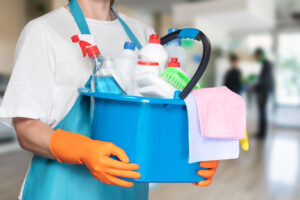 ffice Cleaning Services Bloomington IL, A person wearing gloves holds a bright blue bucket filled with various cleaning supplies. The setting appears to be an indoor area, ready for a thorough cleaning session.